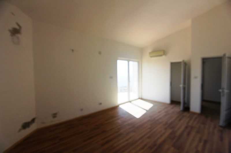 Bright living room with laminate flooring and access to the balcony in a villa in Dobra Voda, Montenegro. Empty room for renovation.