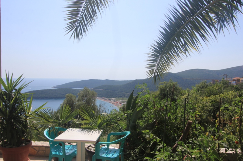 Blick von der Terrasse des Hauses in Seoce, Montenegro: Tisch mit Kunststoffstühlen, Palmen und Panoramablick auf das Meer und die Berge.