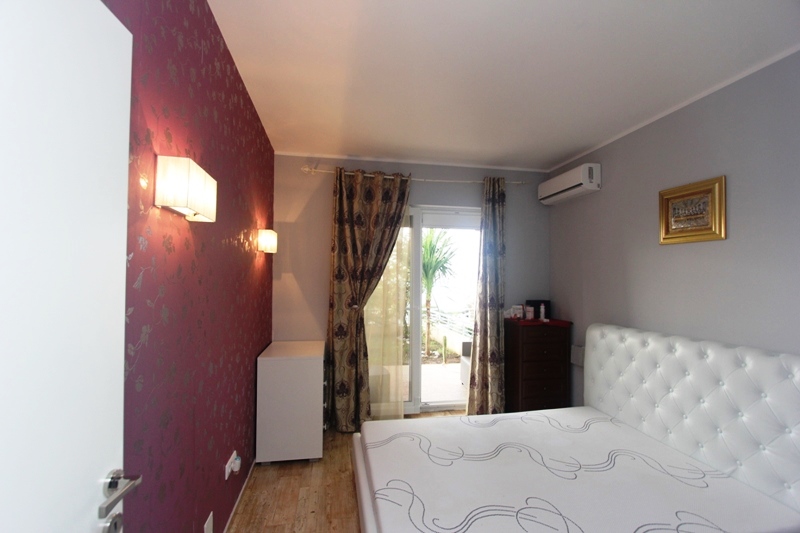 Schlafzimmer mit weißem Bett, Akzentwand in Bordeaux und Zugang zur Terrasse in einem Haus, Stadt Uteha, Montenegro.