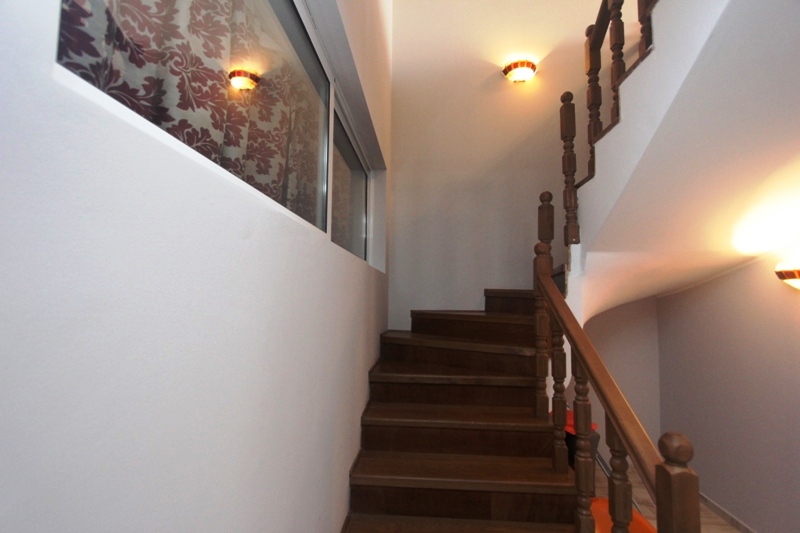Holztreppe mit geschnitztem Geländer in einem Haus in Utjeha, Montenegro, helles Interieur mit Wandleuchten.