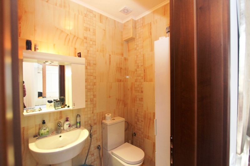 Badezimmer in einem Haus in Utjeha, Montenegro: beige Fliesen, Waschbecken, Spiegel mit Beleuchtung und Sanitäranlagen.