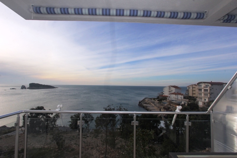 Panoramablick auf das Meer und die Insel vom Balkon des Hauses in Utjeha, Montenegro: Glasgeländer und Sonnenschutz.