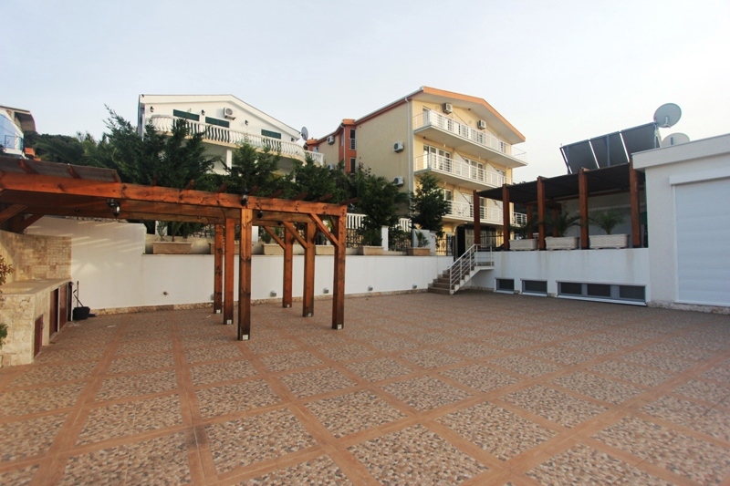 Geräumige Terrasse mit hölzerner Pergola und Grillbereich am Haus in Utjeha, Montenegro. Blick auf die Wohnanlage.