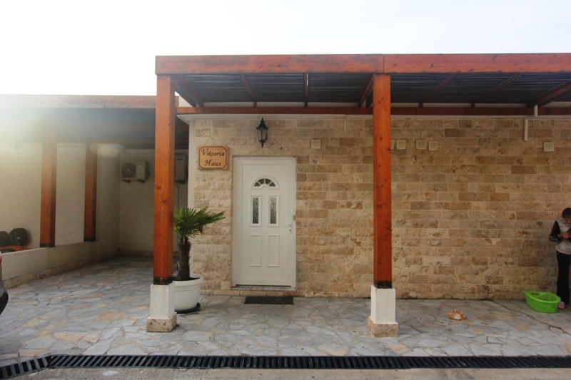Fassade des Hauses Viktoria Haus in Uteha, Montenegro: Steinverkleidung, überdachte Terrasse mit Holzstützen und Eingangstür.