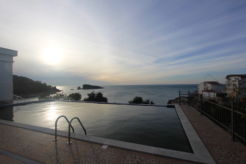 Offener Pool mit Panoramablick auf das Meer und die Insel im Ort Utjeha, Montenegro. Terrasse mit Fliesen am Pool.