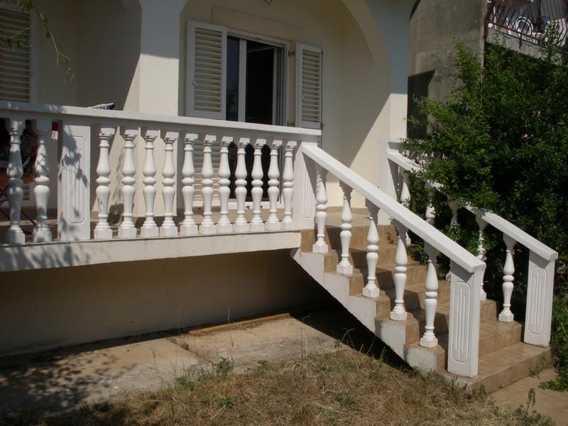 White terrace with balustrade and stairs by the house in Baošići, Montenegro. House entrance with tile and white shutters.