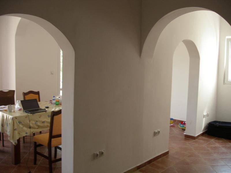 Living room interior in a house in Baošići, Montenegro: light walls, arched openings, and tiled flooring in the dining area.