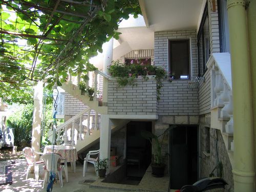 Gemütliche Terrasse eines Hauses in Bečići, Montenegro, mit Weinlaube, Steintreppe und Sitzbereich im Garten.