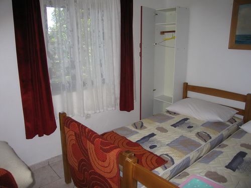 Schlafzimmer mit zwei Einzelbetten und Kleiderschrank in einem Haus in Bečići, Montenegro. Heller Raum mit Fenster und Vorhängen.