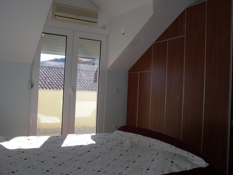 Spavaća soba u potkrovlju kuće u Budvi, Crna Gora: bračni krevet, ugradni ormar i izlaz na terasu.