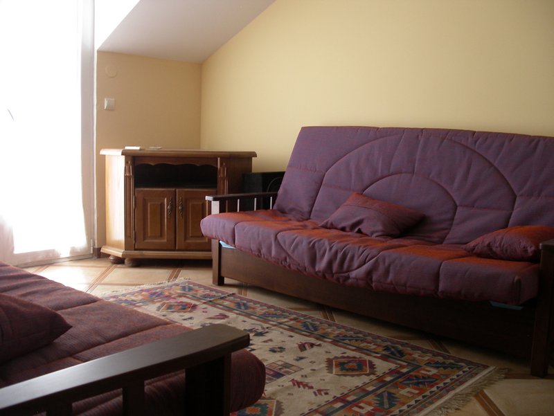 Dnevna soba u kući u Budvi, Crna Gora: ljubičasta sofa, drvena komoda, šareni tepih i svetli zidovi.