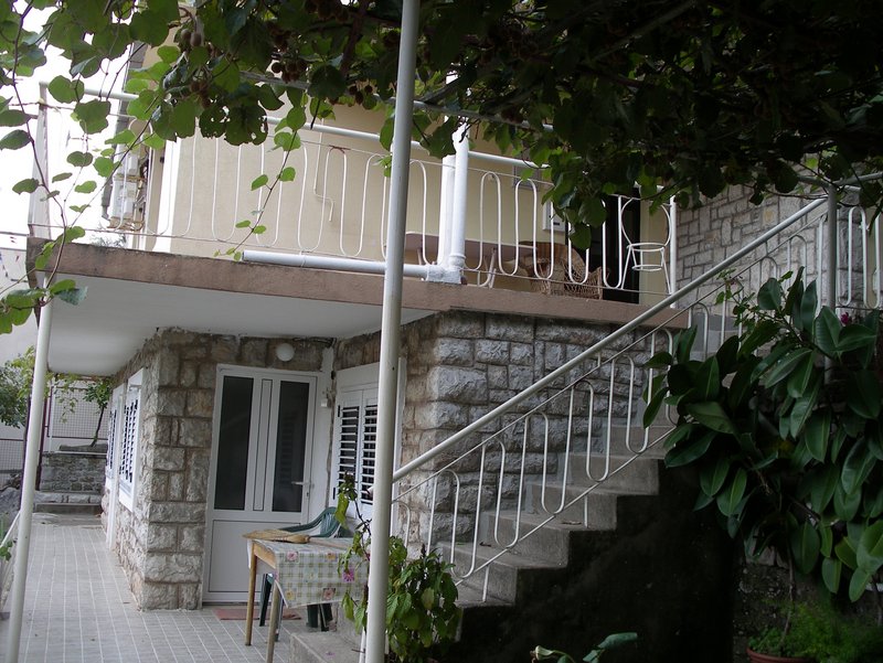 Zweistöckiges Haus in Petrovac, Montenegro: Steinverkleidung der Fassade, offene Terrasse und Treppe in einem grünen Garten.