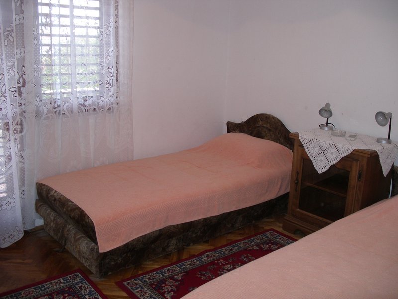 Schlafzimmer in einem Haus in Petrovac, Montenegro: Einzelbett, Holz-Nachttisch, Parkett und Teppiche auf dem Boden.