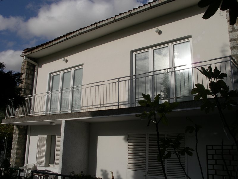 Fassade des Hauses in Petrovac, Montenegro: zweistöckiges Gebäude mit Balkon, Panoramafenstern und Steinverkleidung der Wände.