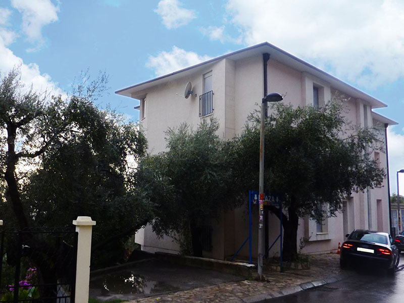Dreistöckiges Wohnhaus in Sveti Stefan, Montenegro, mit Olivenbäumen und Parkplätzen vor der Fassade des Gebäudes.