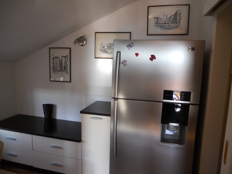Moderne Küche in einer Wohnung in Budva, Montenegro: LG-Kühlschrank, weiße Unterschränke mit schwarzer Arbeitsplatte und Wanddekoration.