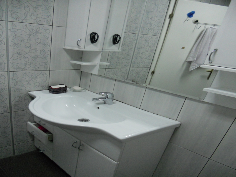 Badezimmer in einer Wohnung in Budva, Montenegro: weiße Waschtischkommode mit Waschbecken, Spiegel und Fliesen mit Blumenmuster.