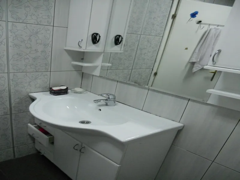 Badezimmer in einer Wohnung in Budva, Montenegro: weiße Waschtischkommode mit Waschbecken, Spiegel und Fliesen mit Blumenmuster.