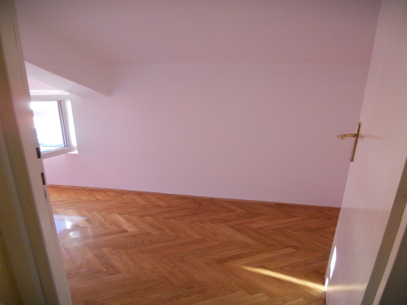 Helles, leeres Schlafzimmer mit Parkettboden und Fenster in einer zum Verkauf stehenden Wohnung in Budva, Montenegro.