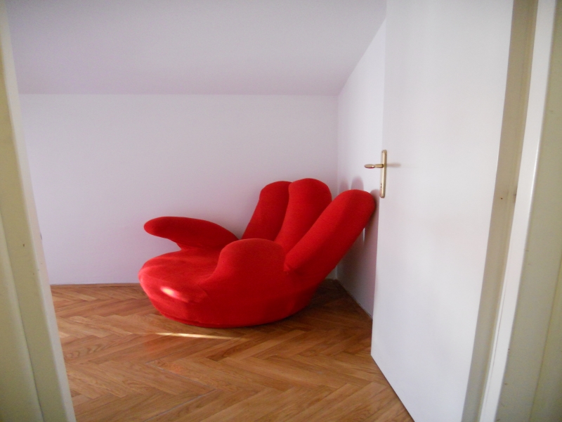 Heller roter Designer-Sessel im Wohnzimmer einer Wohnung in Budva, Montenegro, mit Parkettboden und weißen Wänden.