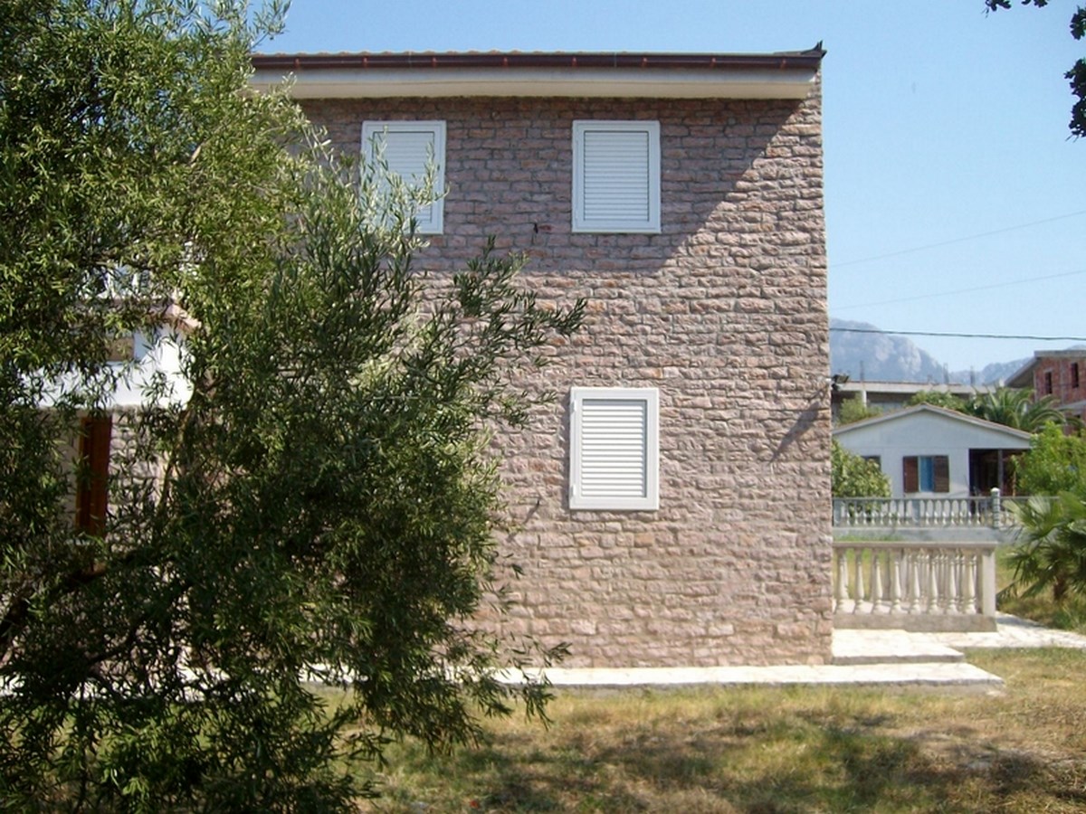 Steinhaus Außenbereich mit weißen Fenstern und grünem Baum