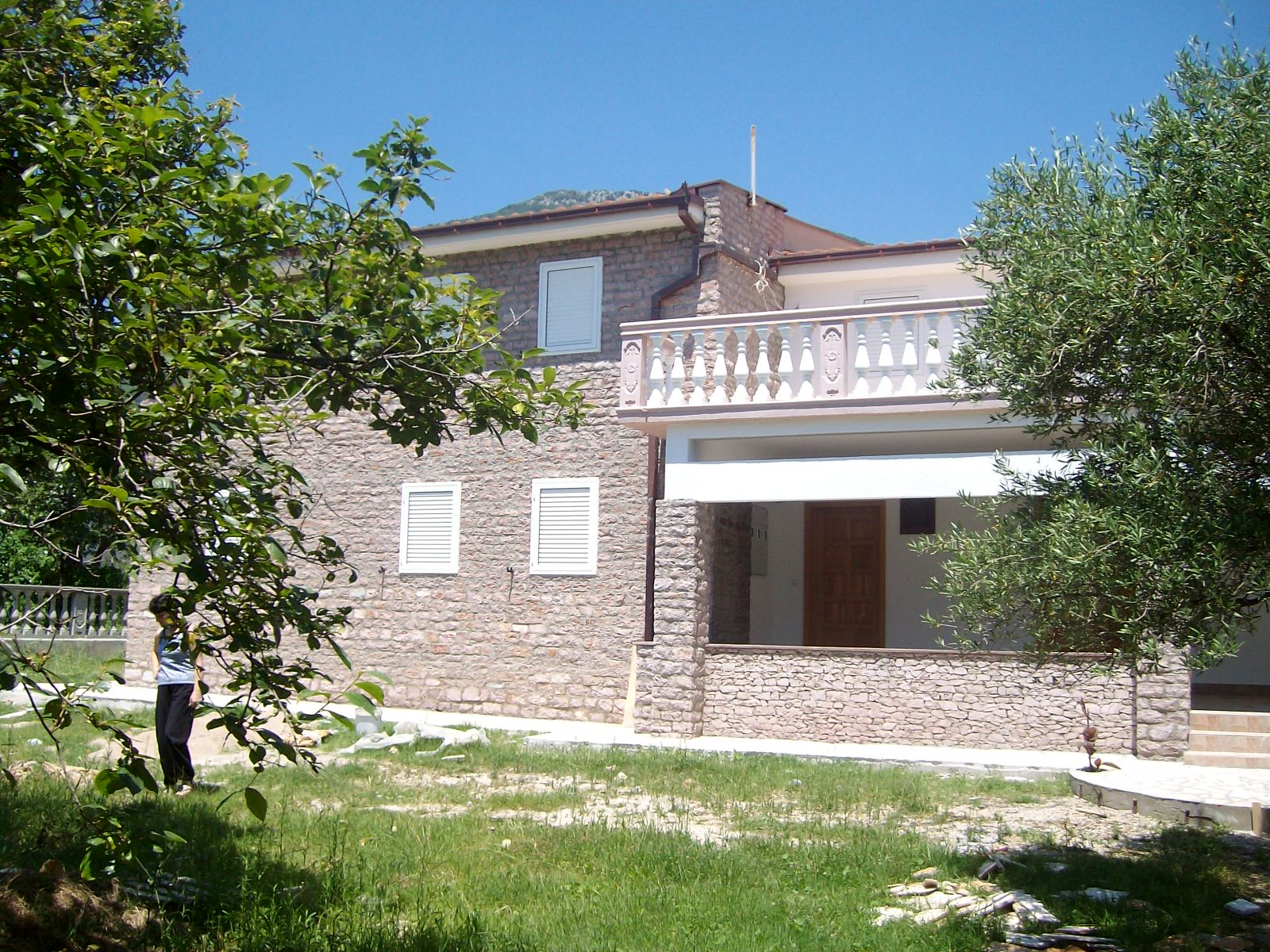 Ein zweistöckiges Steinhaus mit Balkon und umgebendem Grün.
