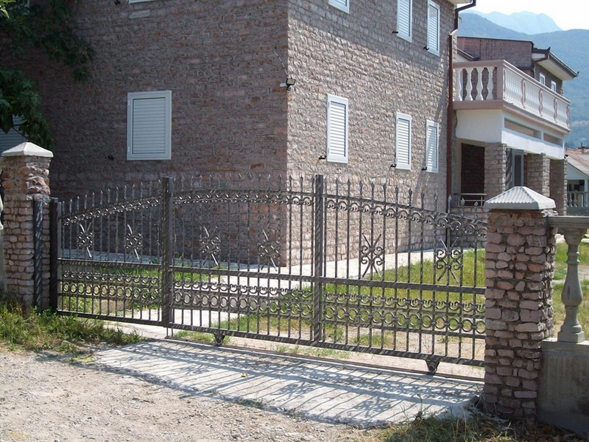 Steinhausfassade mit einem verschnörkelten Metalltor und Pfeilern.