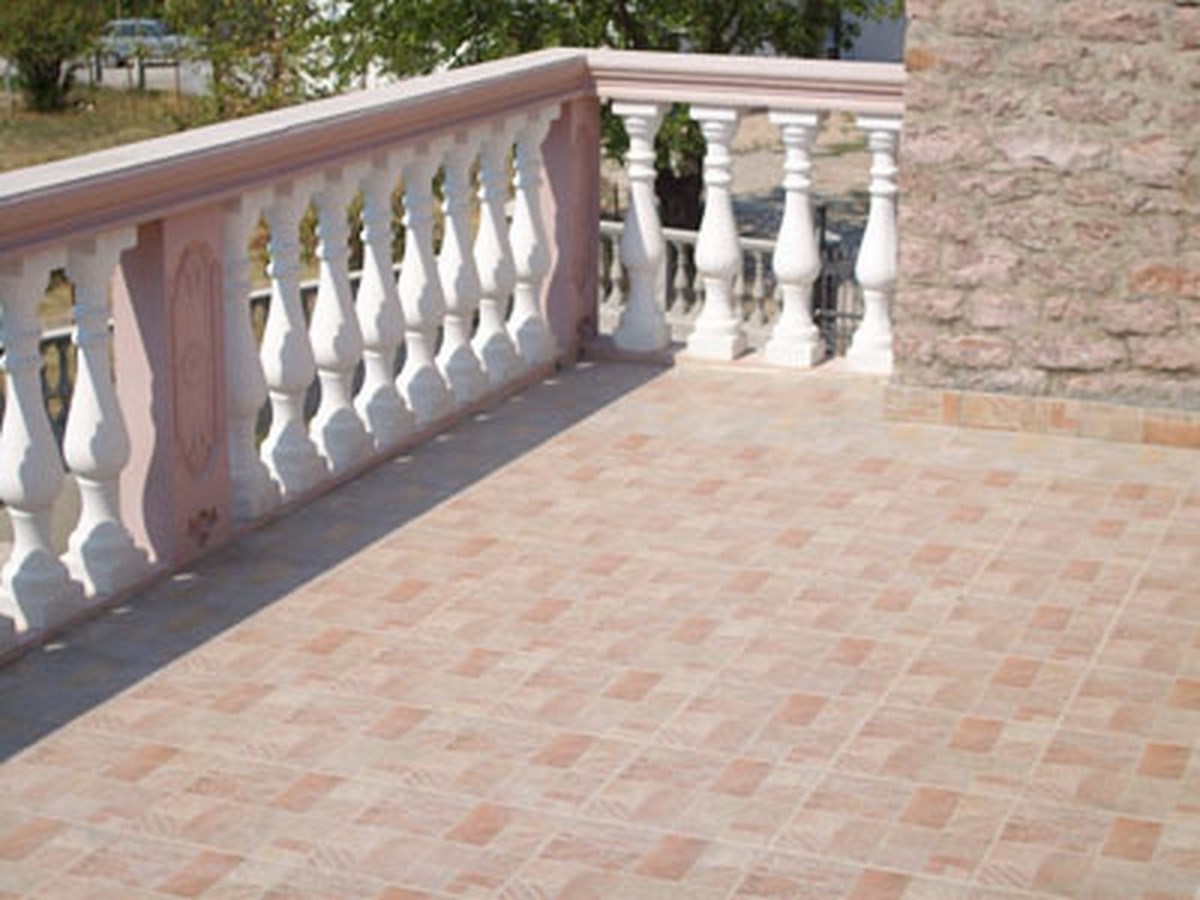 Ein gefliester Balkon mit weißer Balustrade und einer Steinwand.