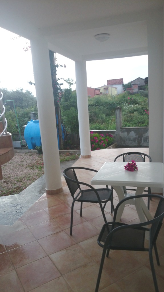 Überdachte Terrasse mit weißen Säulen und Gartenmöbeln in einem Haus, Stadt Shushan, Montenegro. Blick auf den grünen Garten und die Berge.
