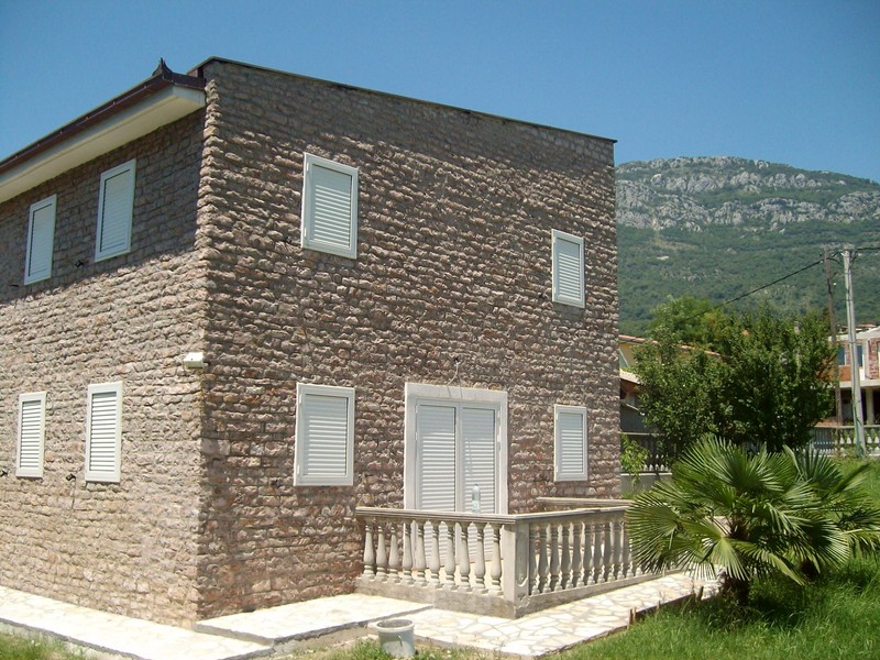 Ein zweistöckiges Steinhaus mit Balkon und Bergen im Hintergrund