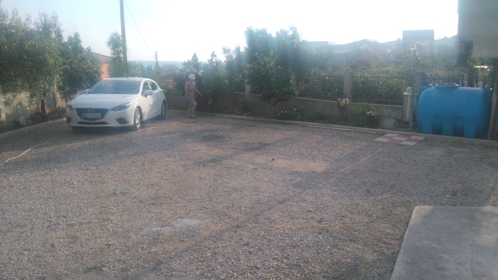 Privater Parkplatz am Haus in Šušanj, Montenegro: Kiesfläche, Auto und Wassertank auf dem Grundstück.
