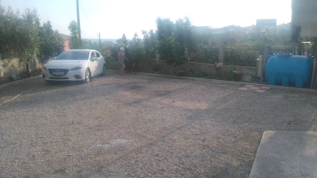 Schotterhof mit einem geparkten weißen Auto, einer Person und einem Wassertank.