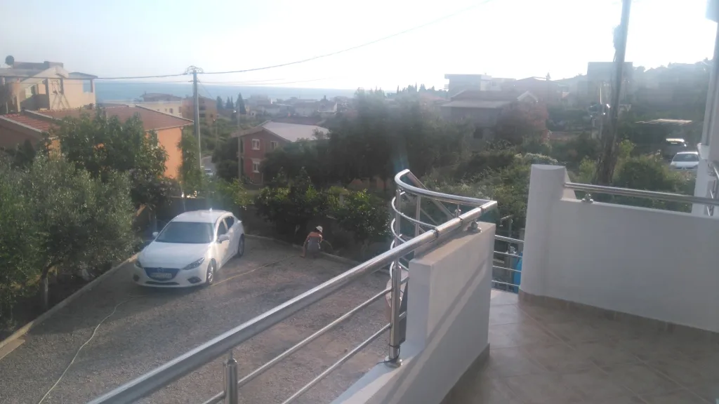 Blick von einem breiten Balkon auf einen Hof mit weißem Auto und die Stadt.