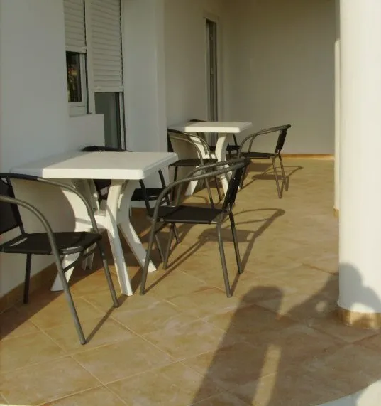 Ein Balkon mit zwei weißen Tischen und schwarzen Metallstühlen.