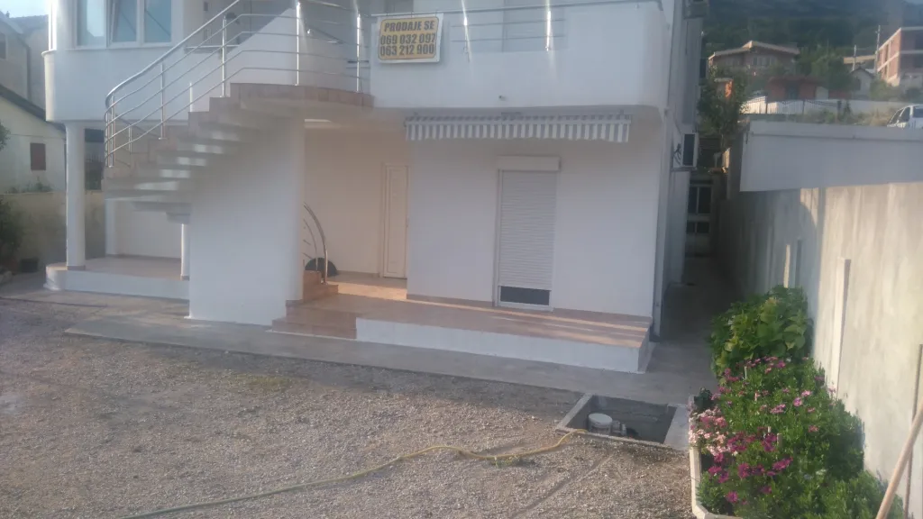Außenansicht eines weißen Hauses mit Außentreppe und einem Verkaufsschild.