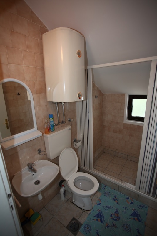 Badezimmer in einem Haus in Dobri Vody, Montenegro: Fliesen, Duschkabine, Sanitäranlagen und Boiler im Dachgeschoss.