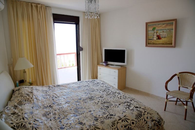 Helles Schlafzimmer mit Doppelbett, TV und Zugang zum Balkon in einem Haus in Dobri Vody, Montenegro.