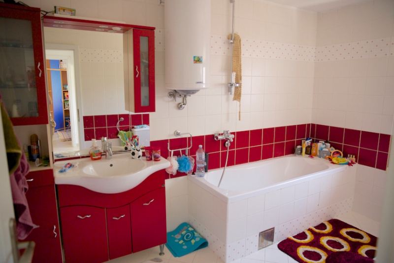 Badezimmer mit roten Möbeln, weißen Fliesen und Boiler in einem Haus zum Verkauf, Dobri Vody, Montenegro.