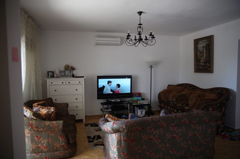 Gemütliches Wohnzimmer mit Polstermöbeln und TV in einem Haus zum Verkauf, Dobri Vody, Montenegro. Heller Innenraum mit schmiedeeinem Kronleuchter.