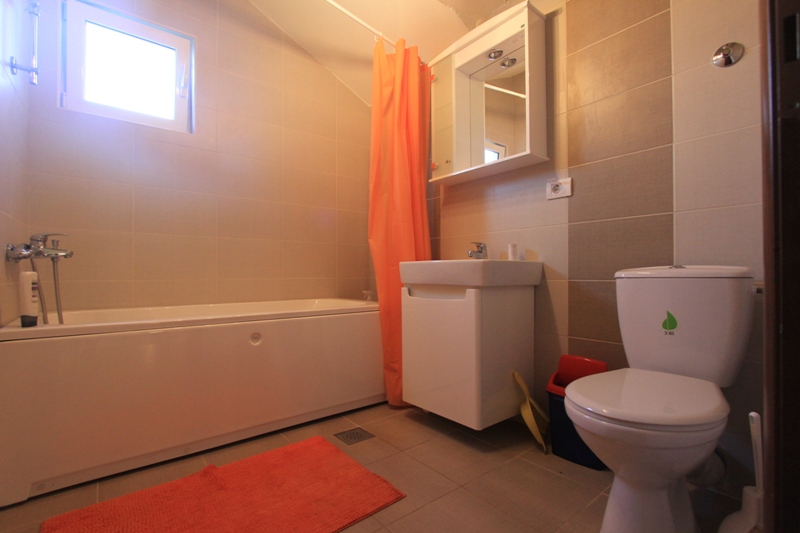 Badezimmer mit weißer Sanitärkeramik und Fliesen in einer Villa in Lepetani, Montenegro: Badewanne, Waschbecken und Toilette.