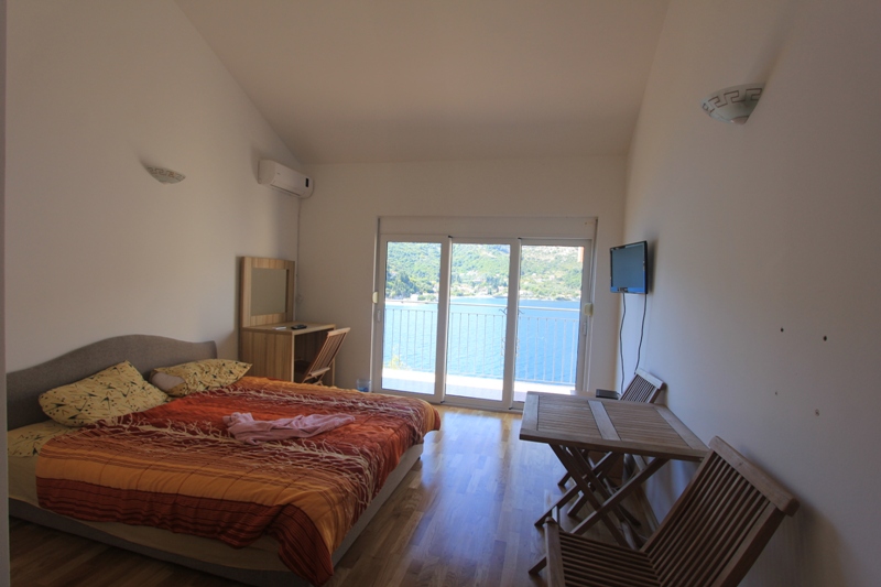 Schlafzimmer in der Villa Lepetani, Montenegro: Doppelbett, Holzmöbel und Panoramablick auf das Meer aus dem Fenster.