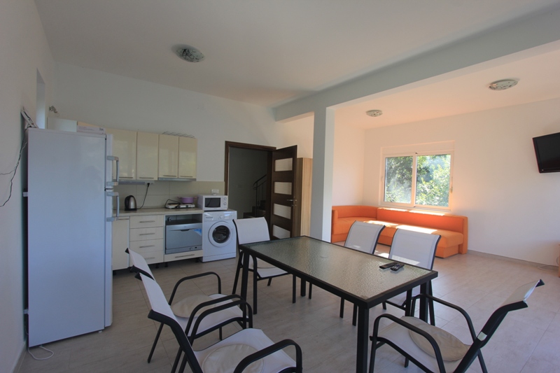 Wohnzimmer mit Küche in einer Villa in Lepetane, Montenegro: Essbereich, helle Möbel, orangefarbenes Sofa und Haushaltsgeräte.