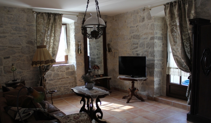 Wohnzimmer in einem Steinhaus in Strp, Montenegro: Vintage-Möbel, Natursteinwände und Fliesenboden.