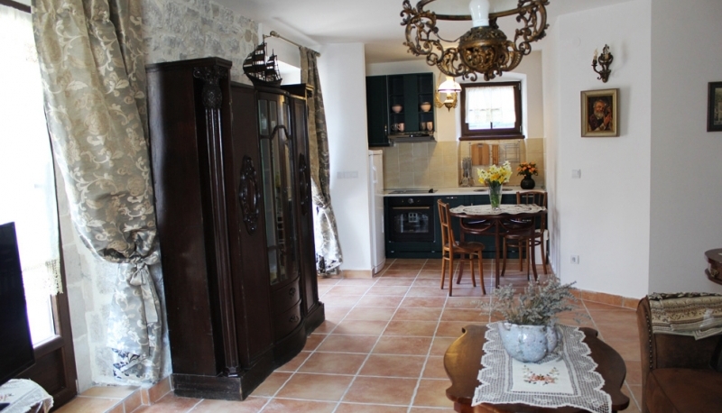Innenraum des Wohnzimmers mit Küche in einem Haus in Strp, Montenegro: Steinwand, antiker Schrank, Fliesenboden und gemütliche Möbel.
