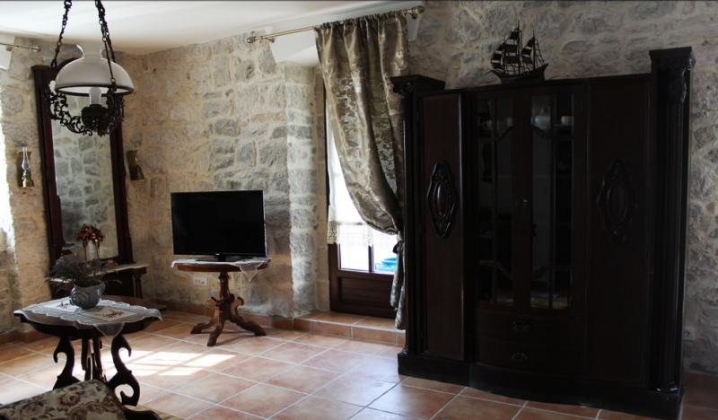 Wohnzimmer in einem Steinhaus in Strp, Montenegro: antike Möbel, Natursteinwände und Fliesenboden.