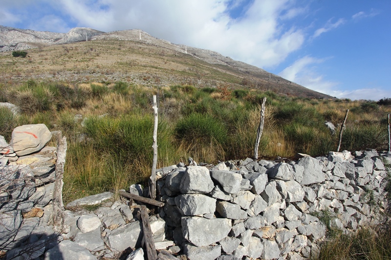 Grundstück in Reževići, Montenegro: Blick auf die Berglandschaft mit traditioneller Steinmauer und trockenem Gras.