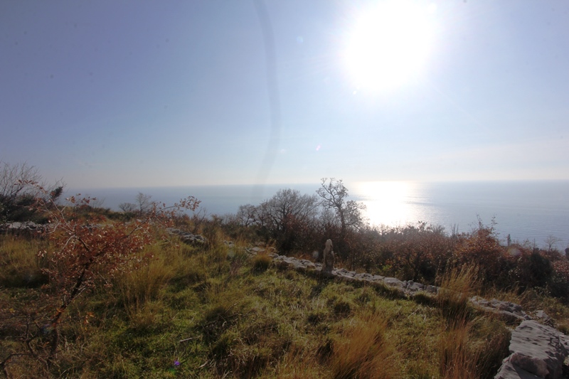 Panoramablick auf die Adria vom Grundstück in Reževići, Montenegro, mit Steinmauer und hügeliger Landschaft.