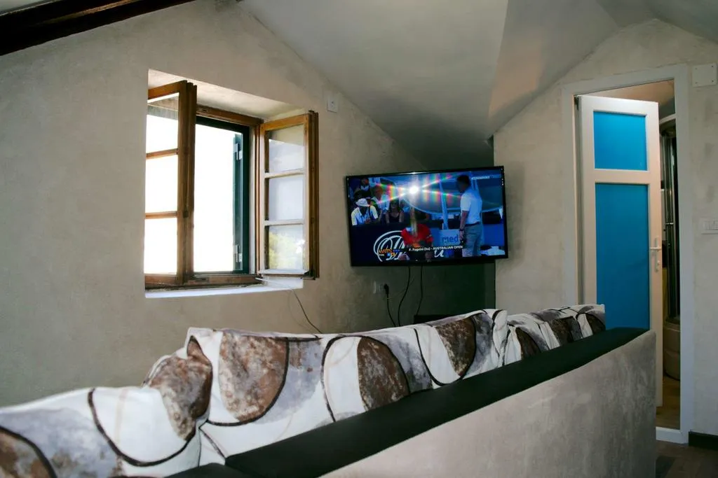 Wohnzimmer in einem Haus in Dobrota, Montenegro: gemütliches Sofa, Wand-TV und Fenster mit heller Wandverkleidung im Interieur.
