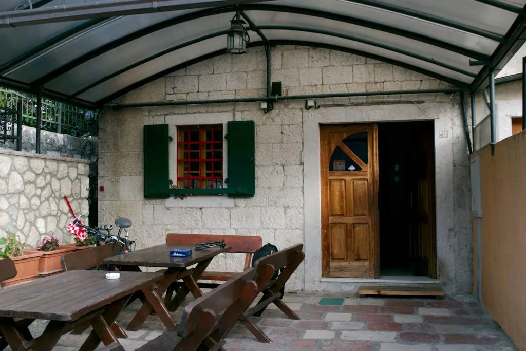 Steinhaus in Dobrota, Montenegro: Terrasse mit Holzmöbeln, Überdachung und traditionellen grünen Fensterläden.