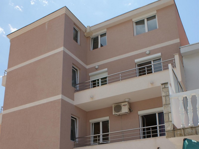 Karadağ, Budva’daki modern üç katlı otelin cephesi; balkonlar, panoramik pencereler ve dış cephe kaplaması.